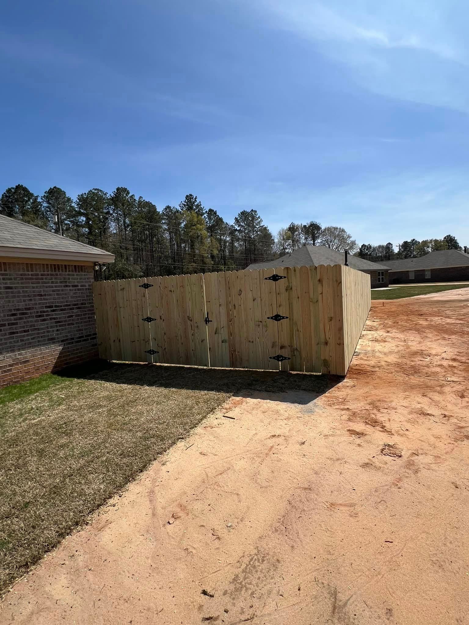 A wooden fence is sitting on the side of a dirt road next to a house.