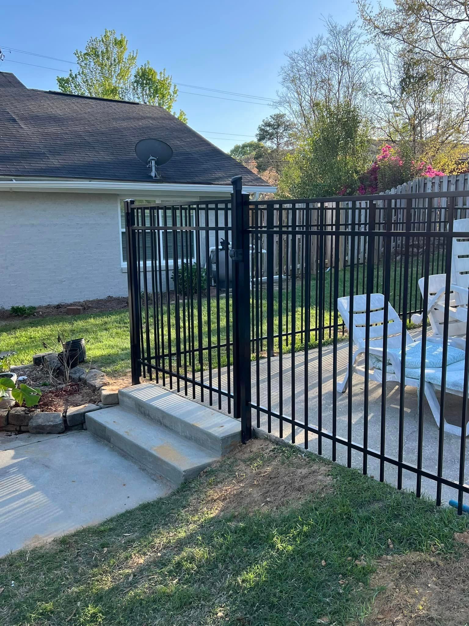 Black metal fence surrounds a patio with steps leading up to it. A house is in the background.