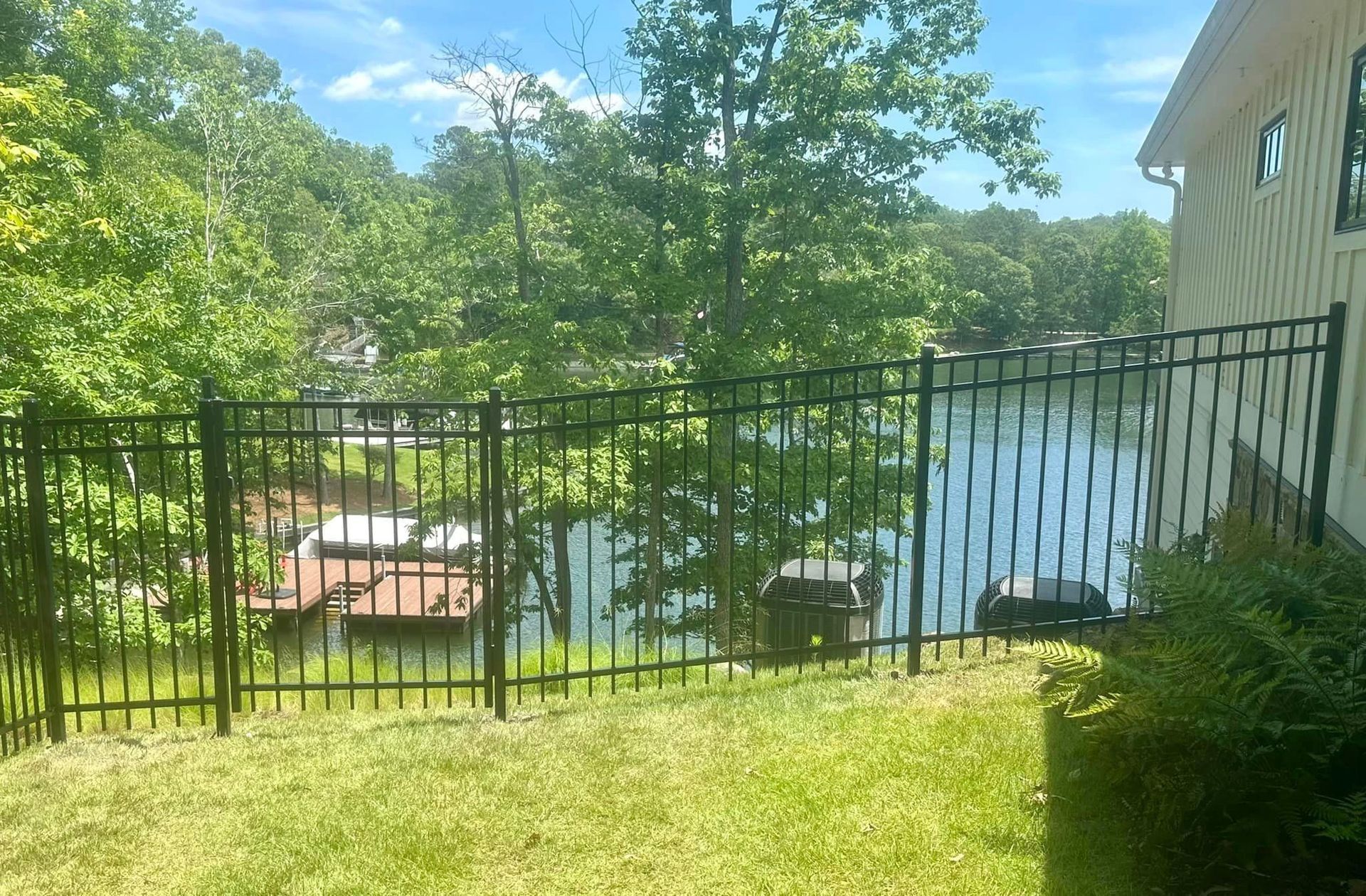 A black fence surrounds a yard with a view of a lake.
